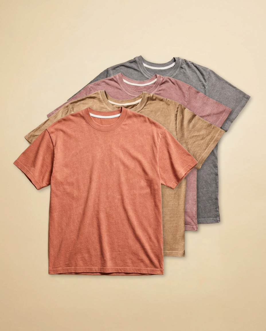 Four folded combed cotton t-shirts in assorted neutral colors, stacked together.