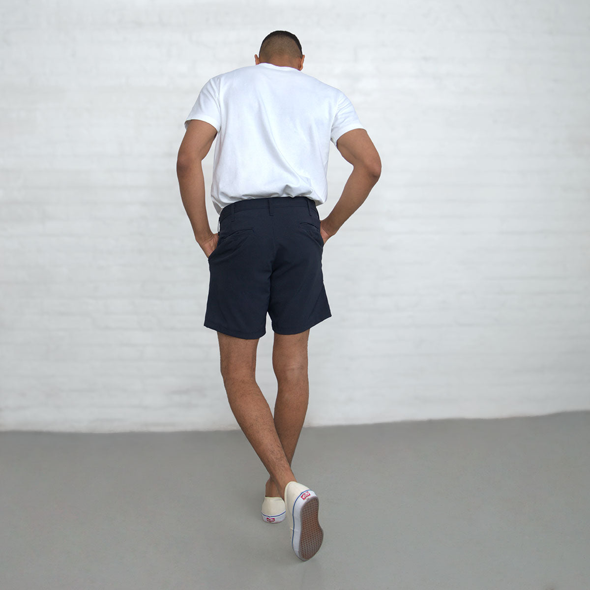 Model seated to show the stretch and fit of the navy technical shorts through the thigh.
